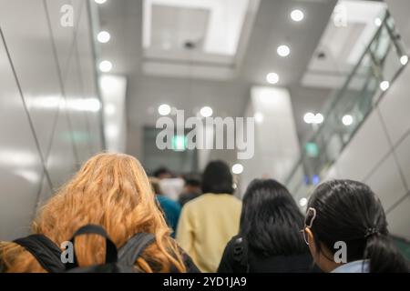 Un groupe de personnes marche dans un couloir. Une femme porte un sac à dos Banque D'Images
