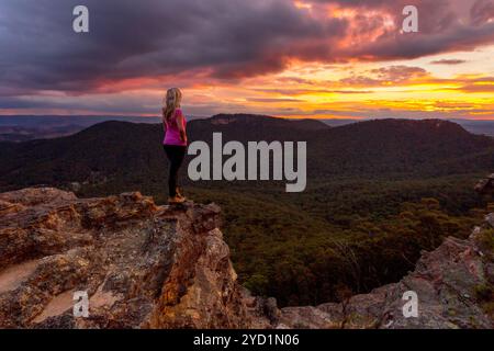 Les nuages d'orage planent au-dessus des Blue Mountains et des vallées alors que le soleil se couche. Une femme se tient sur le précipice rocheux en profitant des vues magnifiques Banque D'Images