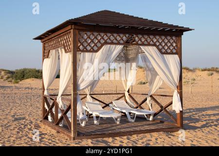 Gazebo sur la plage au bord de la mer. Plage de sable. Les rideaux se développent dans le vent. Banque D'Images