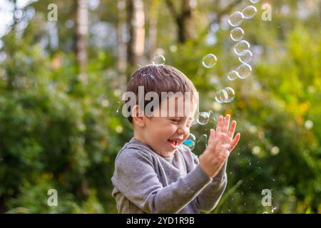 Un garçon dans la rue attrape des bulles de savon. Heureuse enfance. Jeux pour enfants. Banque D'Images