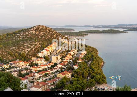 Les maisons aux toits rouges du paisible village côtier reposent le long d'une colline verdoyante, avec vue sur les eaux calmes et les îles lointaines. Banque D'Images