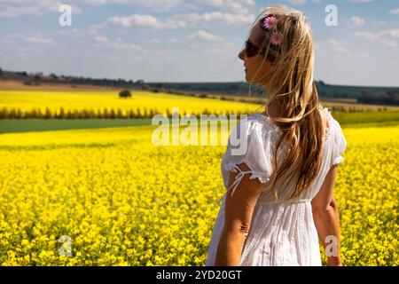 Femme en robe blanche debout par des champs de canola doré Banque D'Images