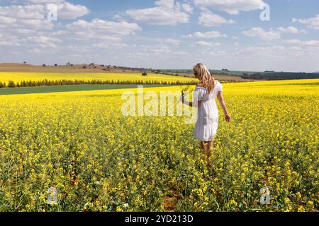 Femme parmi un champ de plantes de canola fleurissant au soleil de printemps Banque D'Images