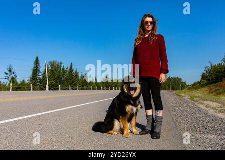 Femme avec chien posant sur l'autoroute. Fier propriétaire avec son chien et le bouvier bernois. Forêt et environnement naturel dans la backgorund. Banque D'Images