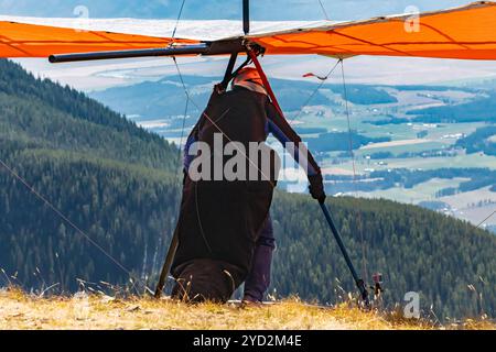 Homme avec deltaplane se préparer à voler du sommet de la montagne. Parapente en haut de la colline. Un pilote de plan Delta sur le point de se lancer Banque D'Images