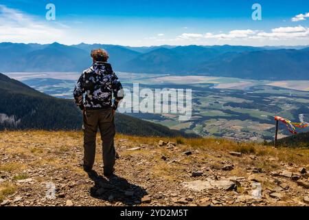 L'homme regarde autour de la colline. Guy se dresse au sommet de la montagne et jouit d'une vue panoramique sur la vallée de Kootenay, Creston, Colombie-Britannique, Canada Banque D'Images