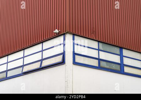 Une seule caméra de surveillance est montée sur le coin d'un bâtiment industriel rouge avec des fenêtres au cadre bleu Banque D'Images