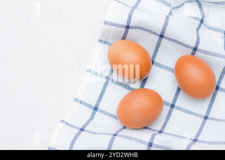 Oeufs de poule sur une serviette de cuisine à carreaux sur une table lumineuse. concept de produits agricoles et d'aliments naturels. Article sur les produits pour la maison Banque D'Images