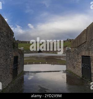 Pompéi, Italie, 25 novembre 2023 : vue de l'amphithéâtre et entrée avec reflets dans une flaque d'eau dans l'ancienne ville de Pompéi, en Europe Banque D'Images