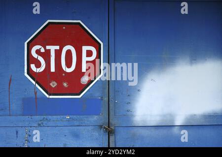 Un panneau d'arrêt rouge sur un bleu verrouillé porte d'un entrepôt désaffecté with Copy Space Banque D'Images