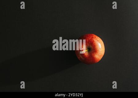 Pomme rouge formant une ombre contre le dos noir Banque D'Images