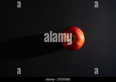 Pomme rouge formant une ombre contre le dos noir Banque D'Images