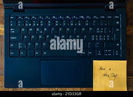 Un clavier d'ordinateur portable avec une note autocollante jaune qui dit « bonne journée ». L'ordinateur portable est ouvert et le clavier est noir Banque D'Images