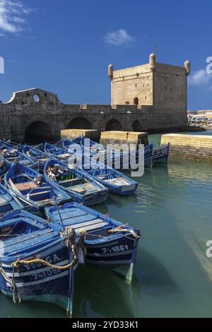 Essaouira, Maroc, 26 mars 2024 : la tour de guet Borj el Barmil et les bateaux de pêche bleus colorés dans le vieux port d'Essaouira, en Afrique Banque D'Images