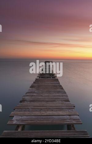 Un lever de soleil vertical paysage marin avec un vieux quai en bois menant dans les eaux calmes de l'océan Banque D'Images