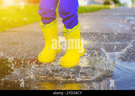 Mes pieds bottés de caoutchouc rebondissent dans une flaque d'eau. Article sur les bottes en caoutchouc. Chaussures d'été pour enfants. Flaques d'eau après la pluie. Mauvais wea Banque D'Images