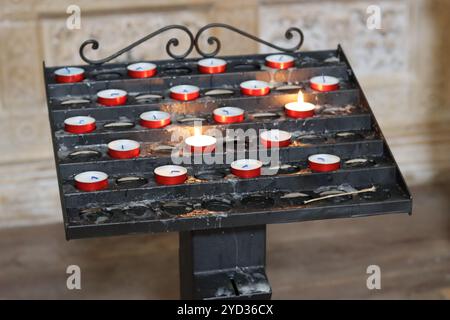 Stand votif dans une église remplie de petites bougies rouges Banque D'Images