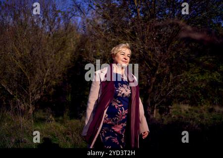 femme âgée avec les cheveux gris en manteau beige clair appréciant la nature dans la forêt d'automne Banque D'Images