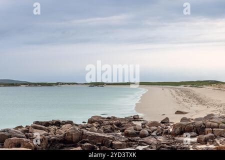 Une figure solitaire se promène le long de la vaste plage de sable de Gurteen Bay, en Irlande, au coucher du soleil. La scène met en évidence la mer turquoise tranquille, douce sa Banque D'Images