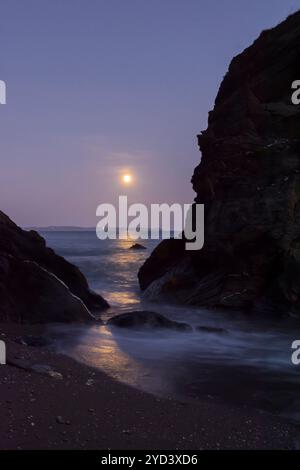 Lever de la lune vu à travers et au-dessus des rochers au bout de la plage de Plaidy près de Looe, Cornwall, Royaume-Uni, 17 septembre 2024, nuit avant Super Harvest Moon, Corn Moon Banque D'Images