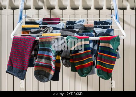 Chaussettes colorées suspendues à la corde à linge séchant sur le radiateur à la maison en hiver. Banque D'Images