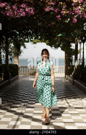 Une femme youbg souriante habillée de vert marche sous une arche de fleurs Banque D'Images