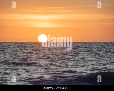 Un petit bateau naviguant sur l'océan alors que le soleil touche l'horizon Banque D'Images