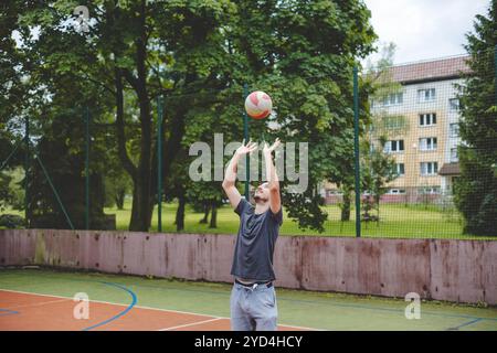 Joueur de volley-ball s'entraînant à placer le ballon sur un terrain dur, en se concentrant sur le contrôle et la précision pendant une séance d'entraînement en plein air. Un m calme et concentré Banque D'Images