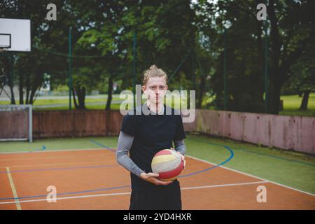 Joueur de volley-ball debout sur un terrain dur, tenant un ballon avec concentration et détermination avant le match. L'image capture un moment calme de préparati Banque D'Images