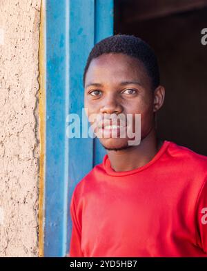 village jeune homme africain, avec un grand sourire dentelé, devant le cadre de porte d'une maison de boue Banque D'Images