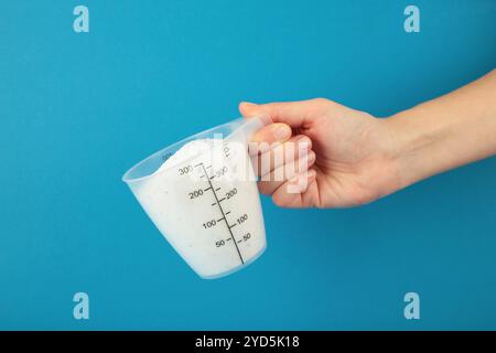 Cuillère à mesurer avec de la poudre à laver à la main sur fond bleu. Vue de dessus Banque D'Images