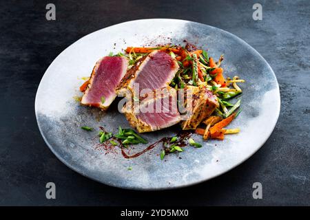 Tataki traditionnel de steak de thon gastronomique japonais avec tranches de légumes et pousses de soja avec sauce douce servie en gros plan sur un motif nordique Banque D'Images