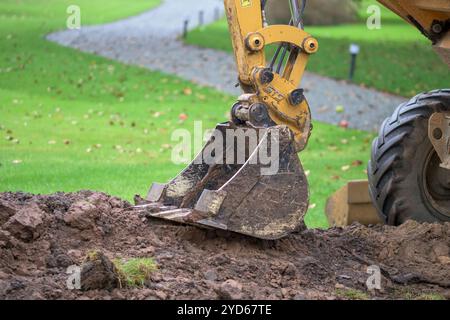 Chantier de construction avec une pelle jaune creusant le sol dans une zone de parc herbeux, idéal pour les projets impliquant l'aménagement paysager, le terrassement, le développement Banque D'Images