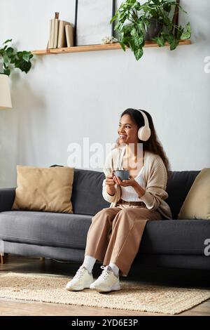 Une femme s'assoit confortablement sur un canapé, souriant tout en écoutant de la musique avec des écouteurs. Banque D'Images