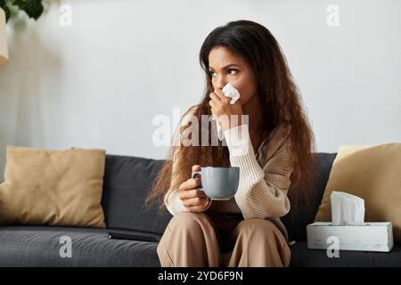 Une jeune femme aux cheveux longs tient une tasse, paraissant pensive tout en se sentant sous les intempéries. Banque D'Images