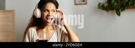 La femme avec des écouteurs sourit largement, tenant un verre de vin rouge dans sa main. Banque D'Images