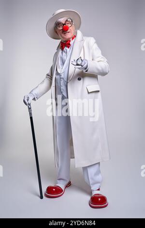 Un clown âgé avec une montre antique sur une chaîne à la main. Habillé d'un manteau blanc, chapeau et grand clown en cuir verni rouge b Banque D'Images