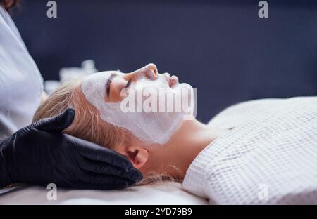 Cosmétologue applique un masque blanc rajeunissant sur le visage de la cliente féminine Banque D'Images