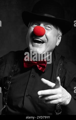 Portrait couleur sélective de clown riant. Habillé en chemise noire avec bretelles, nez de clown rouge et chapeau melon sur la tête Banque D'Images