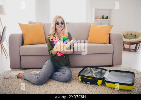 Photo de jolie femme positive assise sur le sol écrivant des plans pour un futur voyage de week-end organisant valise à l'intérieur appartement plat Banque D'Images