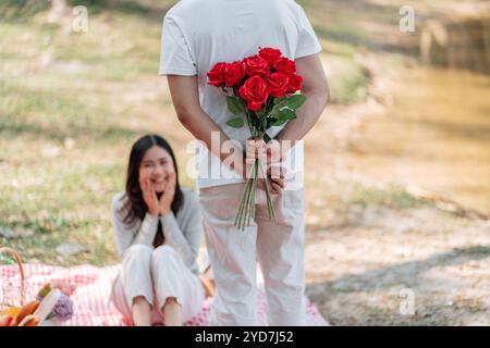 Heureux couple romantique dans la Saint-Valentin homme asiatique cachant la fleur de rose rouge derrière pour surprendre sa petite amie. Banque D'Images