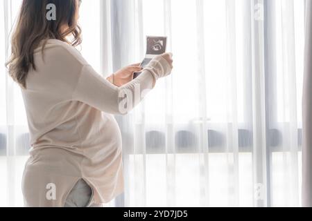 Femme asiatique enceinte tenant l'image de bébé échographique résultat du médecin. Concept de soins de santé de maman heureuse. Banque D'Images