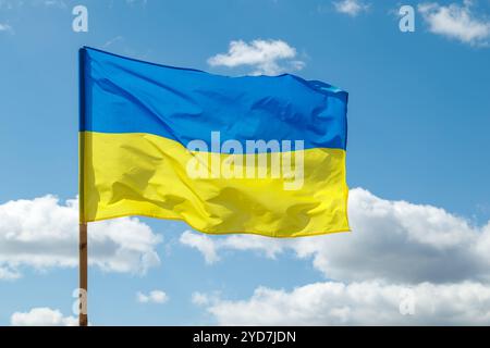 Le drapeau de l'État de l'Ukraine bat dans le vent. Un drapeau jaune et bleu sur un poteau en bois contre un ciel bleu clair par une journée ensoleillée Banque D'Images