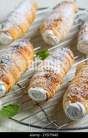 Cornes de pâte feuilletée remplies de crème blanche et de sucre en poudre tombant, mise au point sélective. Banque D'Images