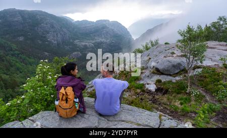 Preikestolen, Norvège deux personnes sont assises sur une montagne rocheuse surplombant une vallée entourée de brume Banque D'Images