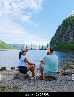 Deux personnes profitent d'un après-midi paisible assis au bord d'un lac serein en Norvège. Le paysage magnifique des montagnes et l'eau bleue claire créent un pict Banque D'Images