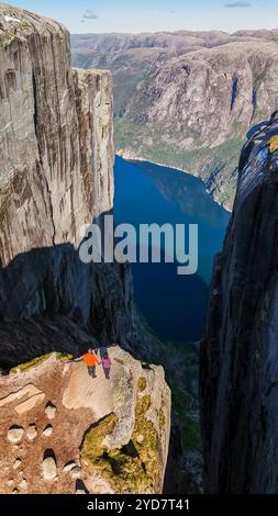 Deux randonneurs se tiennent au bord de Kjeragbolten, en Norvège, une falaise spectaculaire en Norvège, surplombant un magnifique fjord bleu Banque D'Images