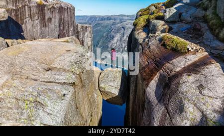 Un randonneur solitaire se tient au bord de l'emblématique falaise de Kjeragbolten en Norvège, contemplant le paysage à couper le souffle en contrebas Banque D'Images