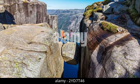 Deux randonneurs se tiennent sur une formation rocheuse au bord de Kjeragbolten, en Norvège, regardant au-dessus de la vaste étendue ci-dessous. Un couple visitant Kjeragbolten Norw Banque D'Images