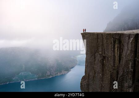 Preikestolen, Norvège Une vue depuis le sommet du Pulpit Rock en Norvège, avec deux personnages debout sur le bord, regardant au-dessus de t Banque D'Images